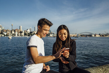 Happy young couple using smart phone while exercising on promenade against Sydney Harbour Bridge - CAVF32325