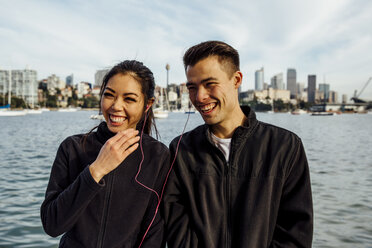 Happy young couple listening music while exercising against cityscape - CAVF32328