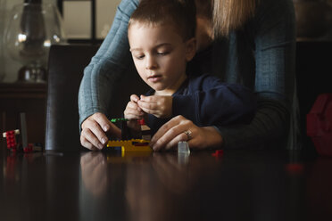 Mittelteil einer Mutter, die ihrem Sohn bei der Herstellung von Spielzeugklötzen am Tisch hilft - CAVF32354