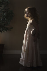 Side view of thoughtful girl holding teddy bear while standing at home - CAVF32356