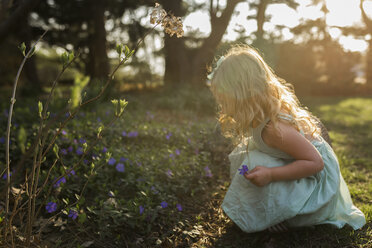 Seitenansicht eines Mädchens, das in der Hocke im Park Blumen pflückt - CAVF32365