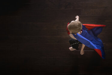 Overhead view of boy wearing superhero cape while walking on hardwood floor - CAVF32370