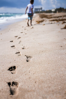 Rückansicht eines Jungen, der Fußspuren hinterlässt, während er auf dem Sand am Strand läuft - CAVF32373