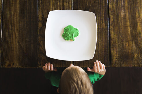 Draufsicht auf einen Jungen mit einem Keks in einem Teller an einem Holztisch - CAVF32375
