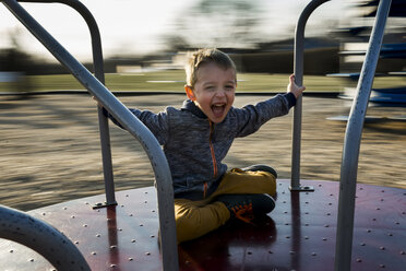 Portrait of cheerful boy sitting on merry-go-round - CAVF32376