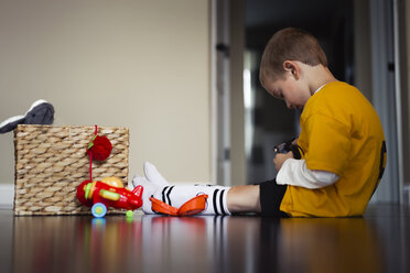 Seitenansicht eines Jungen, der mit Spielzeug spielt, während er zu Hause auf dem Boden sitzt - CAVF32377