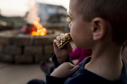 Junge isst Smore im Hof mit Feuerstelle im Hintergrund - CAVF32383