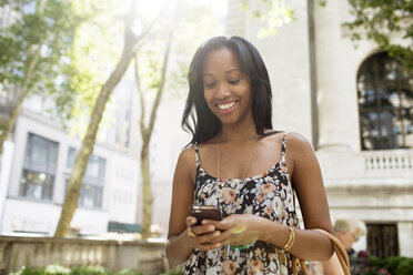 Happy woman text messaging while standing in city - CAVF32426