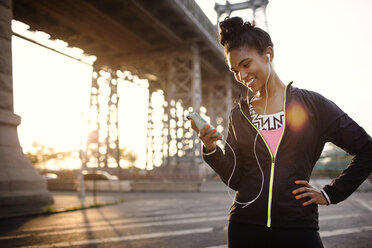 Happy female jogger using phone while standing on city street - CAVF32437