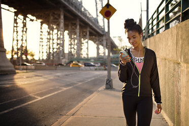 Female jogger text messaging while walking on sidewalk - CAVF32438