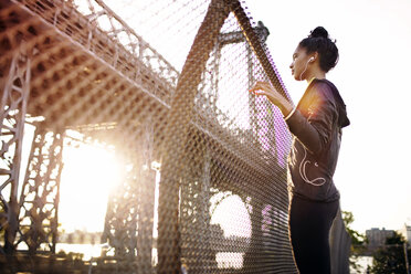 Junge Joggerin mit Blick auf die Williamsburg Bridge an einem sonnigen Tag - CAVF32446