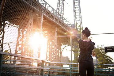 Rückansicht einer Frau, die sich an der Williamsburg Bridge an einem sonnigen Tag streckt - CAVF32451