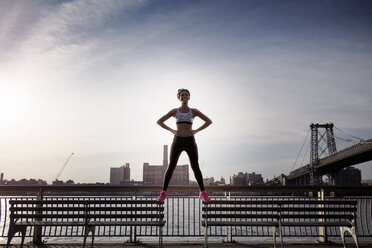 Female jogger with hands on hips standing on benches at promenade - CAVF32456