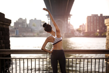 Rear view of sporty woman stretching by railing under Williamsburg Bridge - CAVF32461