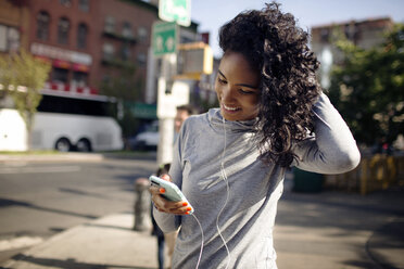 Happy woman using smart phone while standing on street - CAVF32472