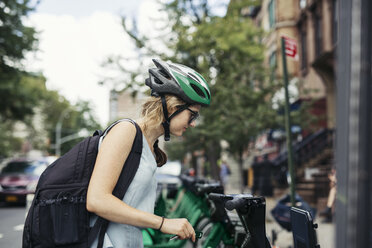 Seitenansicht einer Frau, die ein auf der Straße geparktes Fahrrad betrachtet - CAVF32494