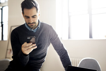 Geschäftsmann, der ein Smartphone benutzt, während er in einem kreativen Büro sitzt - CAVF32525