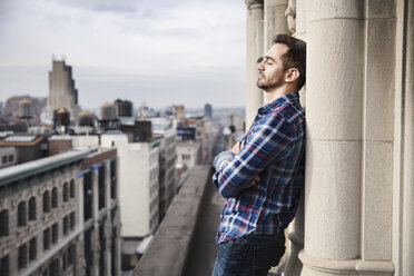 Man leaning on column at balcony against cityscape - CAVF32554