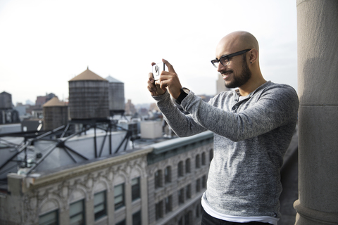 Lächelnder Mann beim Fotografieren mit Smartphone auf dem Balkon, lizenzfreies Stockfoto