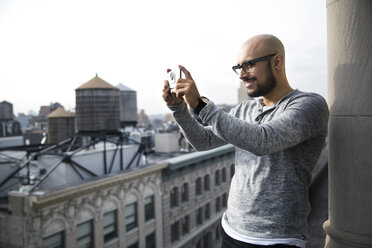 Lächelnder Mann beim Fotografieren mit Smartphone auf dem Balkon - CAVF32564