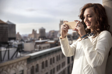 Smiling woman photographing with smart phone on balcony - CAVF32568