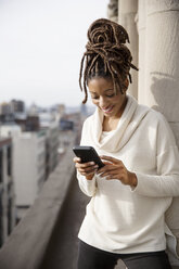 Lächelnde Frau, die ein Smartphone benutzt, während sie auf einem Balkon steht - CAVF32571