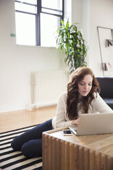 Geschäftsfrau, die einen Laptop benutzt, während sie auf einem Teppich im Büro sitzt - CAVF32573
