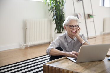 Ältere Geschäftsfrau benutzt einen Laptop, während sie auf einem Teppich im Büro sitzt - CAVF32574
