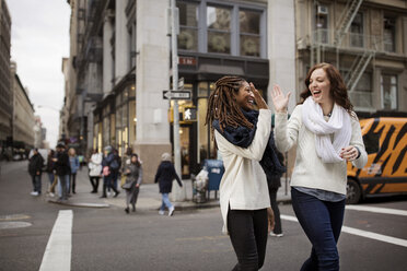 Glückliche weibliche Freunde geben High Five beim Gehen auf der Straße - CAVF32578