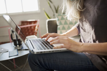 Mittelteil einer Frau, die im heimischen Wohnzimmer einen Laptop benutzt - CAVF32607