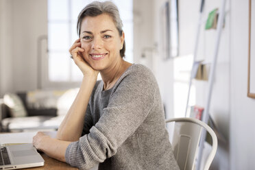 Porträt einer selbstbewussten Frau, die an einem Tisch im Heimbüro sitzt - CAVF32613