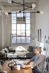 Konzentrierte reife Frau mit Laptop bei der Arbeit am Tisch im Wohnzimmer - CAVF32614