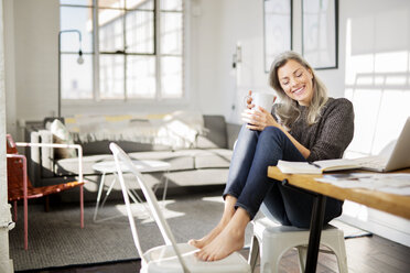 Thoughtful woman holding coffee mug while sitting on chair - CAVF32622