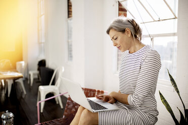 Mature woman using laptop while sitting in living room at home - CAVF32632