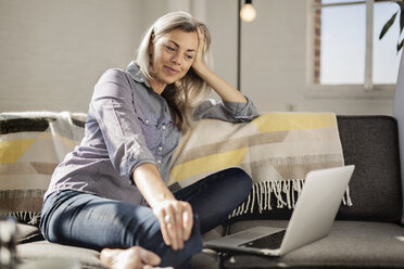 Entspannte Frau mit Laptop auf dem Sofa sitzend - CAVF32641