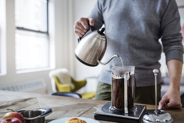 Midsection of man pouring water in French press while preparing coffee at home - CAVF32643