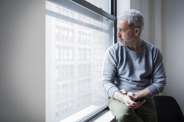 Thoughtful mature man looking through window at home - CAVF32650