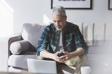 Mature man using laptop while sitting on sofa at home - CAVF32662