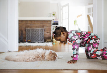 Side view of curious girl looking at cat lying on rug in living room - CAVF32676