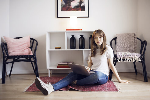 Portrait of young woman sitting with laptop on floor at home - CAVF32691