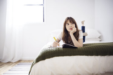 Nachdenkliche junge Frau, die beim Lernen auf dem Bett zu Hause wegschaut - CAVF32692