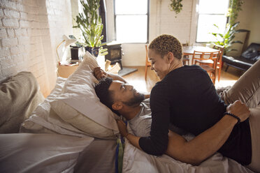 Happy romantic couple looking at each other while lying on bed at home - CAVF32703