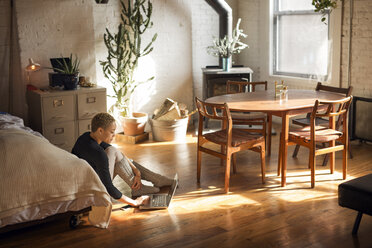 Side view of woman using laptop while sitting on floor in bedroom - CAVF32720