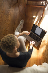 Blick von oben auf eine Frau, die einen Laptop auf einem Hartholzboden im Schlafzimmer benutzt - CAVF32721