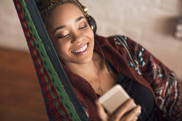 Happy woman listening music through smart phone on hammock at home - CAVF32735