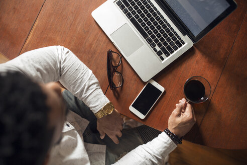 Draufsicht auf einen Mann, der einen schwarzen Kaffee trinkt und einen Laptop am Tisch benutzt - CAVF32751