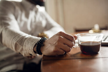 Mittelteil eines Mannes, der eine schwarze Kaffeetasse am Tisch hält - CAVF32752