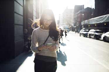 Young woman listening music through smart phone on city street - CAVF32767