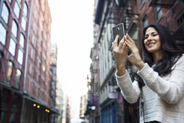 Happy young woman photographing through smart phone in city - CAVF32772