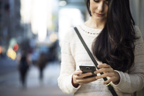 Mittelteil einer jungen Frau, die auf der Straße ein Smartphone benutzt - CAVF32775